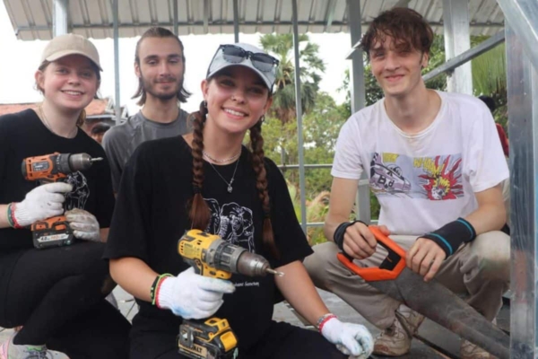 four young people smiling while holding construction tools on a building site