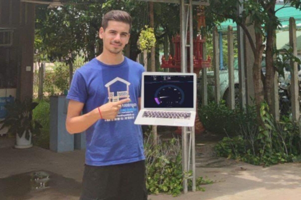 a man holding a laptop standing in front of a residential area with trees