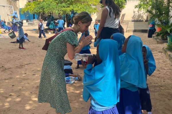 A teacher interacts with young students outdoors, sharing a light-hearted moment in a schoolyard.