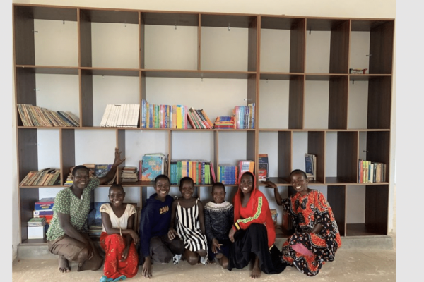 A group of children pose proudly in front of a well-stocked bookshelf, smiling in a library setting.