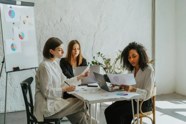 Three interns review charts and data during a meeting in a bright, modern office space.