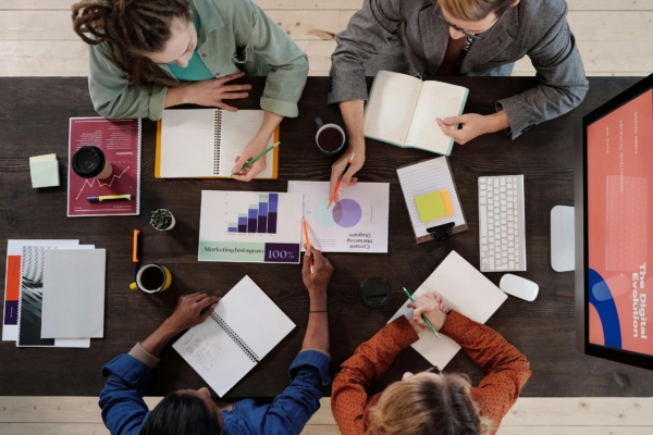 A group of interns collaborate on a marketing project, discussing charts and graphs around a large table.