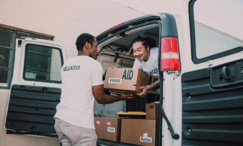 Two interns load aid and food boxes into a van as part of a volunteer project during their NGO internship.