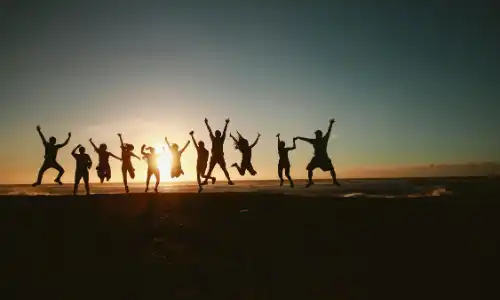 A group of interns jump in excitement on a beach at sunset, silhouetted against the sky, symbolizing teamwork and celebration.