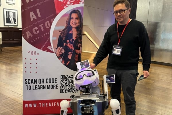 An intern of the robotics internship in Ecuador posing with a robot in front of the banner for the AI factor.