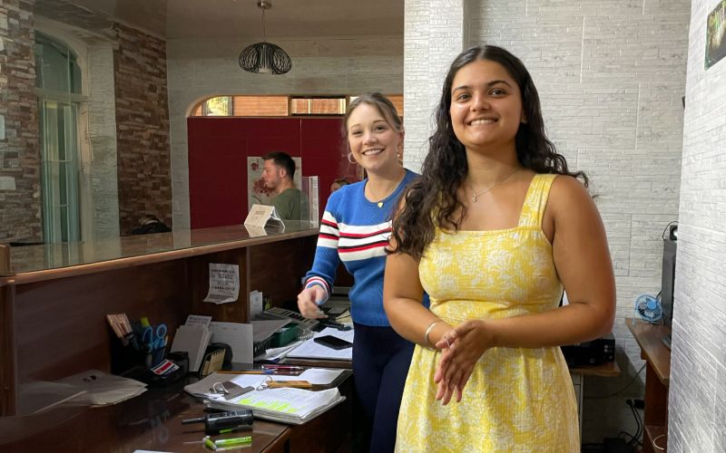 Two interns smiling while working at a reception desk in a tourism office