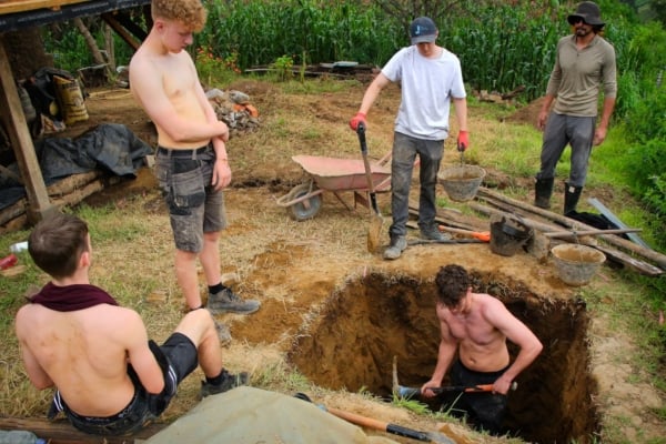 Interns use shovels and tools to dig and clear land for a construction project.