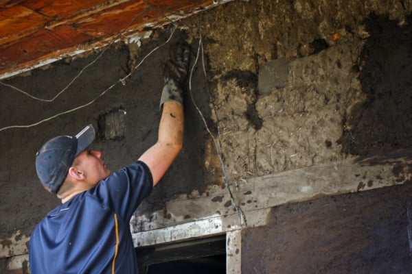 An intern applies a natural mud mixture to reinforce a wall.