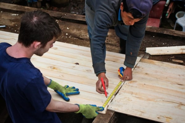 An intern and local builder measure and mark wood for sustainable construction.