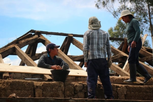 Local builders assess wooden beams during roof construction.