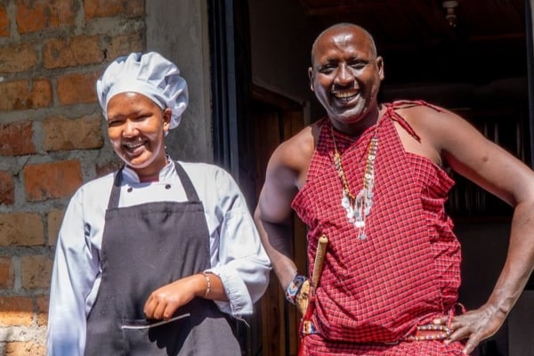 Local hospitality staff member and community leader smiling outside a lodge building, highlighting cultural tourism