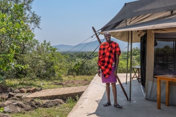 Local tourism host standing outside an eco-friendly safari tent lodge surrounded by natural landscape