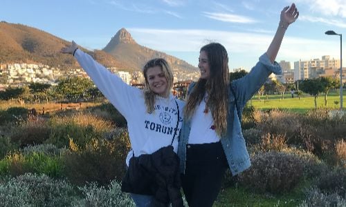 Two friends smiling with arms raised outdoors
