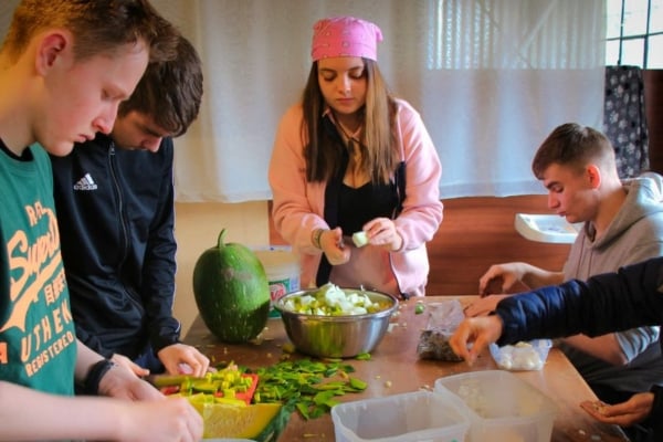 Group of people preparing food together at a table inside a shared kitchen space