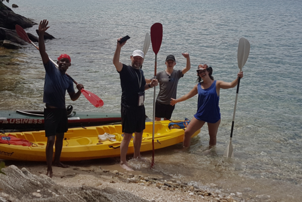Four people standing near a kayak on the beach.