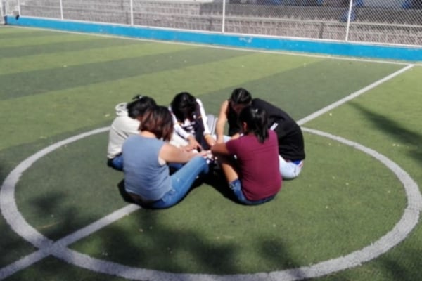 Young women sitting in a circle on an outdoor sports court during a young womens health internship group activity.