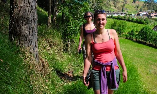 Two people walking along a grassy path through a green hillside on a sunny day