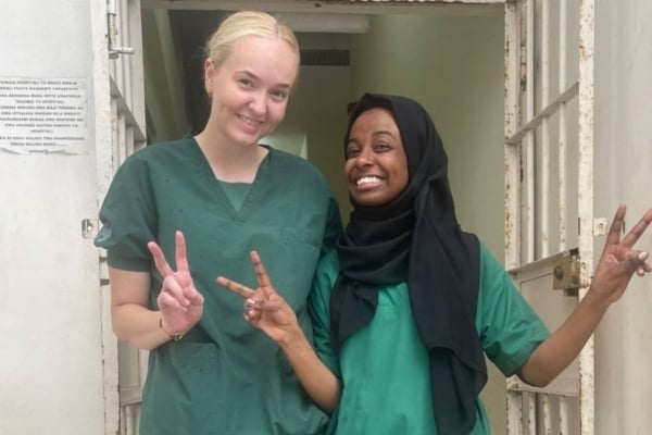 Two women wearing scrubs making peace signs with their hands.